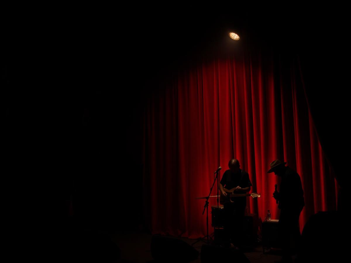 Silhouetted performers on a dim stage lit by a single red-curtained spotlight